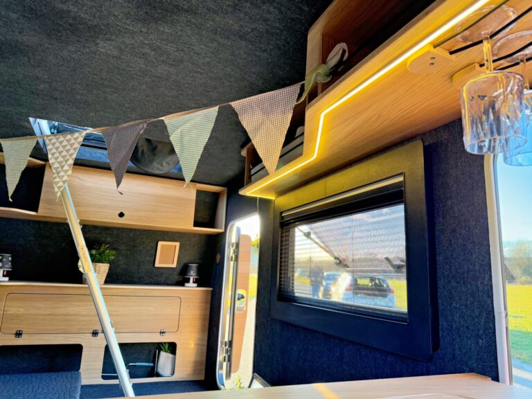Das Interieur dieses Pickup Campers ist ein echtes Allround-Talent: Holzschränke, ein Fenster, eine hängende Pflanze und dekorative Wimpel sorgen für eine individuelle Note. Warmes Licht und Sonnenstrahlen schaffen eine gemütliche Atmosphäre – ideal für grenzenlose Freiheit unterwegs. Dieser Offroad Camper bietet durch sein maßgeschneidertes Design Komfort und Flexibilität auf allen Abenteuern. Egal ob beim nächsten Roadtrip oder abseits befestigter Wege – mit diesem Custom Camper sind Sie perfekt ausgestattet!. Travelboxx - Pickup Wohnkabinen